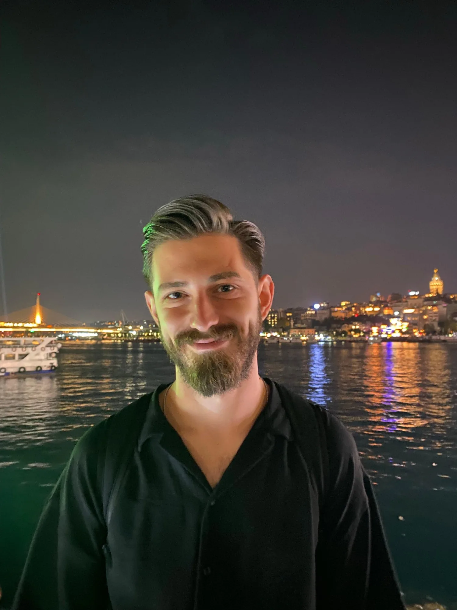 Murat Akkaş gece Haliç'te gülümsüyor; arkada ışıklı Galata Kulesi ve Haliç Metro Köprüsü